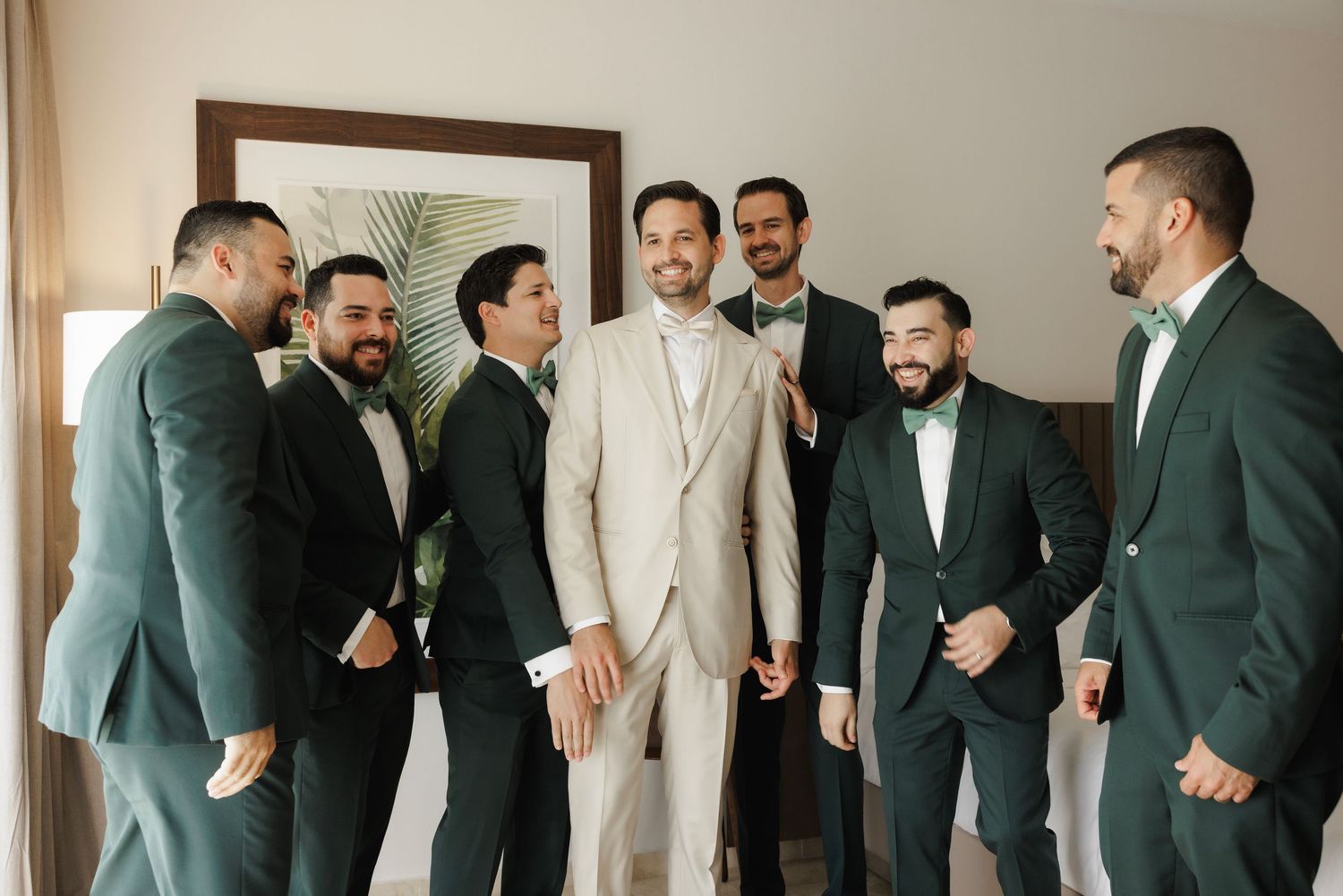 A group of groomsmen in suits chat and laugh together before a wedding ceremony.