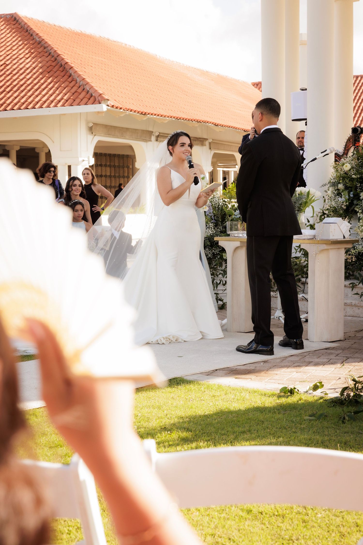 Couple stands together during outdoor wedding ceremony at beautiful Spanish-style venue with white columns.
