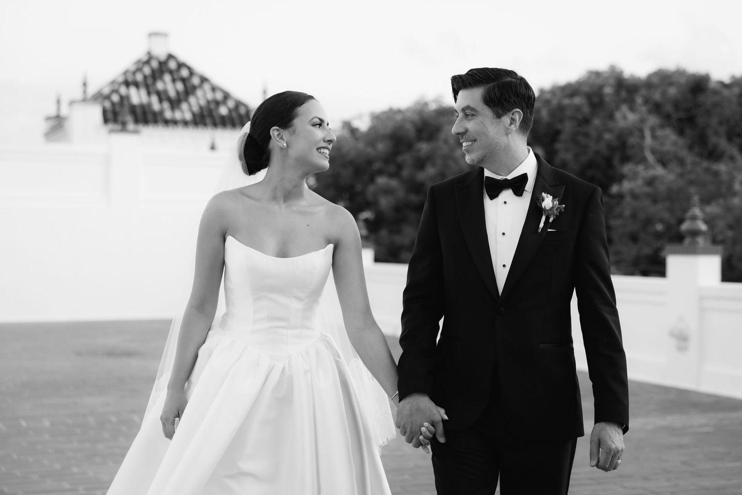 Romantic black and white wedding photo of a couple walking together outdoors.