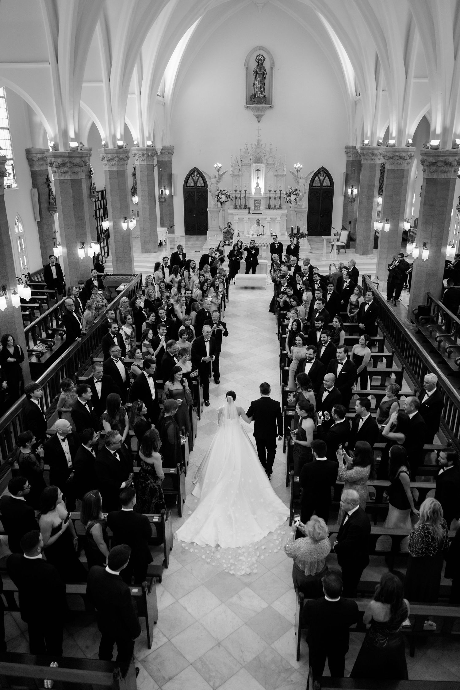 Wedding ceremony in grand cathedral with guests seated in wooden pews.