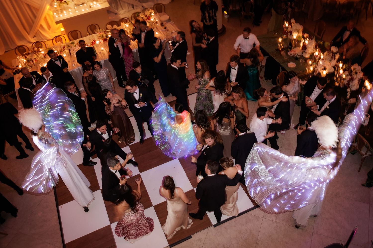 Aerial view of wedding reception dancers with glowing LED wings creating ethereal light patterns on the dance floor.