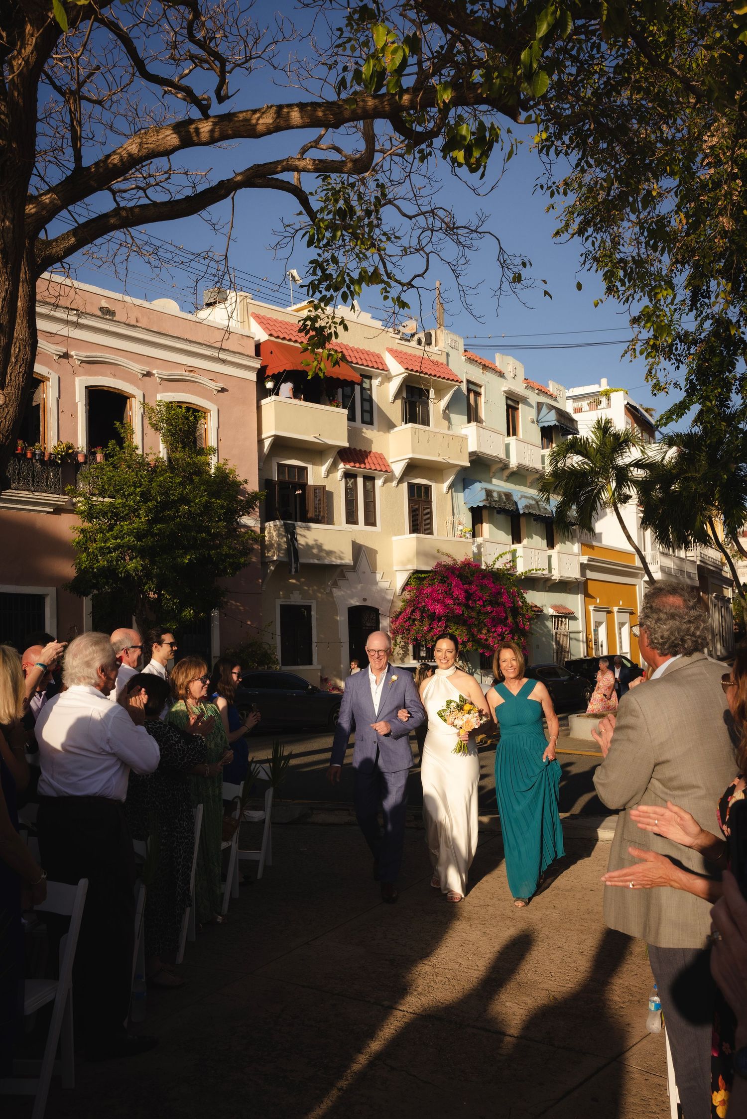 Wedding guests mingling outdoors during golden hour against colonial architecture.