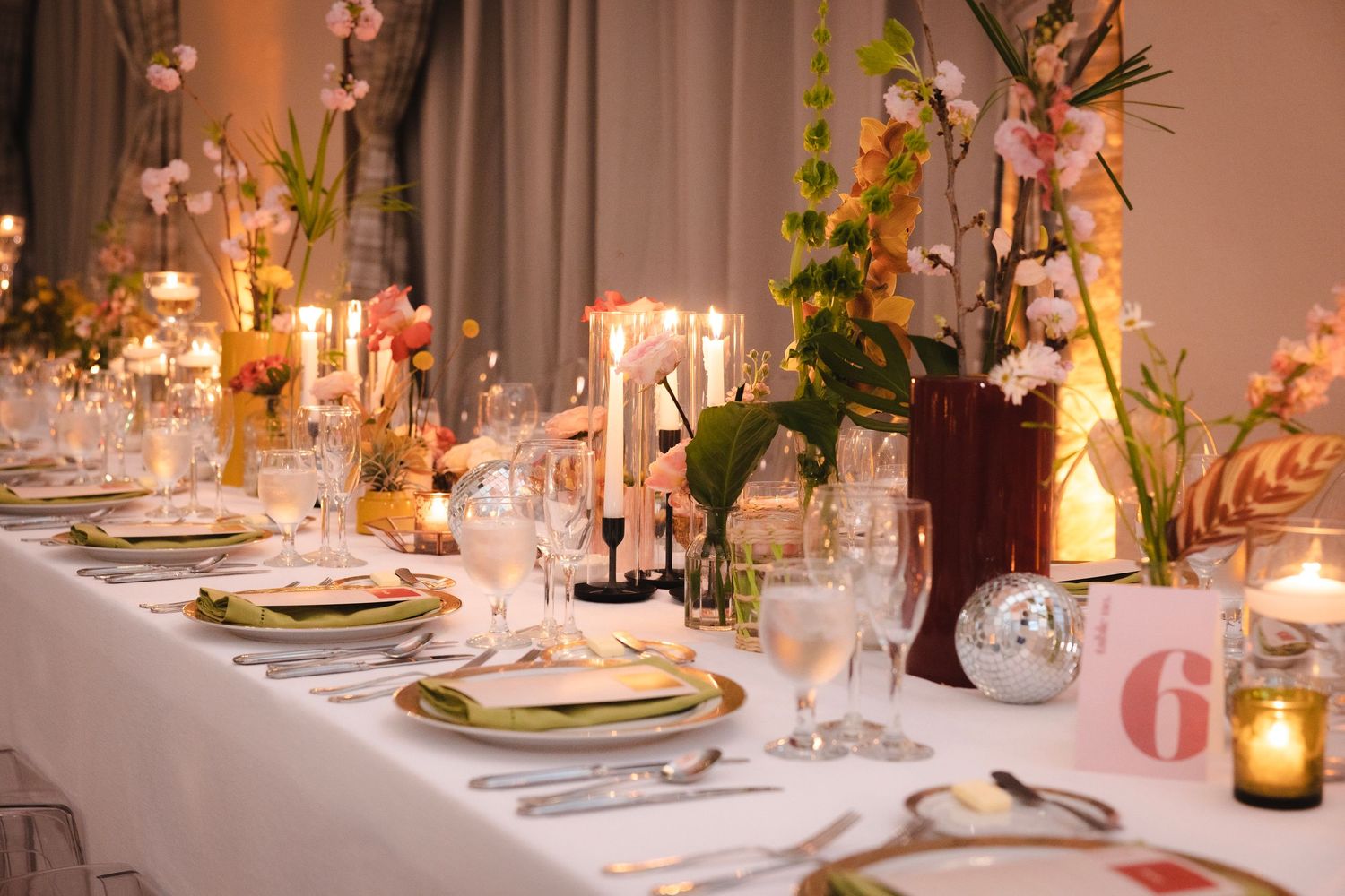 Elegant wedding reception table with white linens, glowing candles, and floral centerpieces in glass vases.