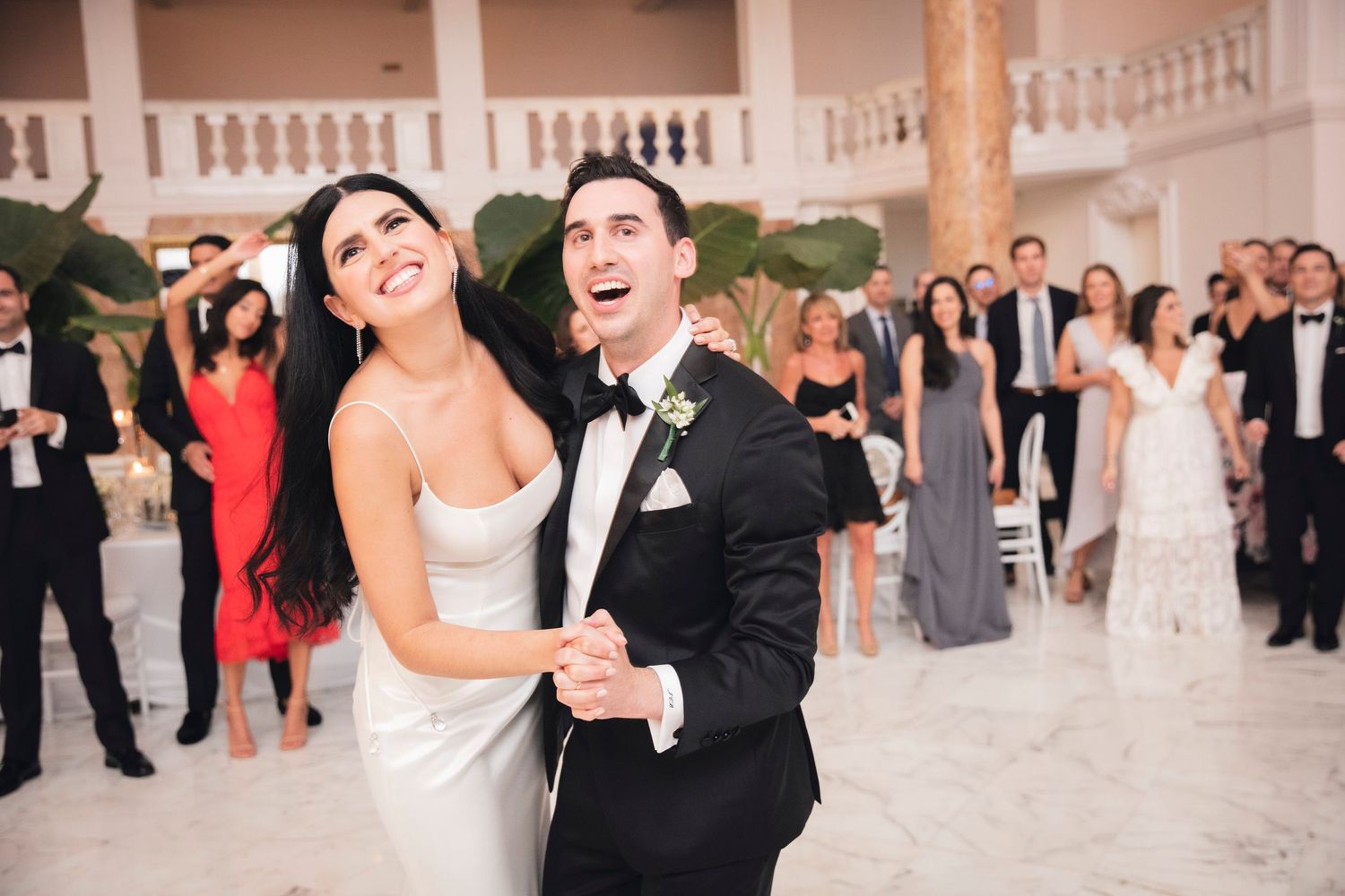 Wedding reception guests dancing and celebrating on an ornate ballroom floor with classic architectural details.