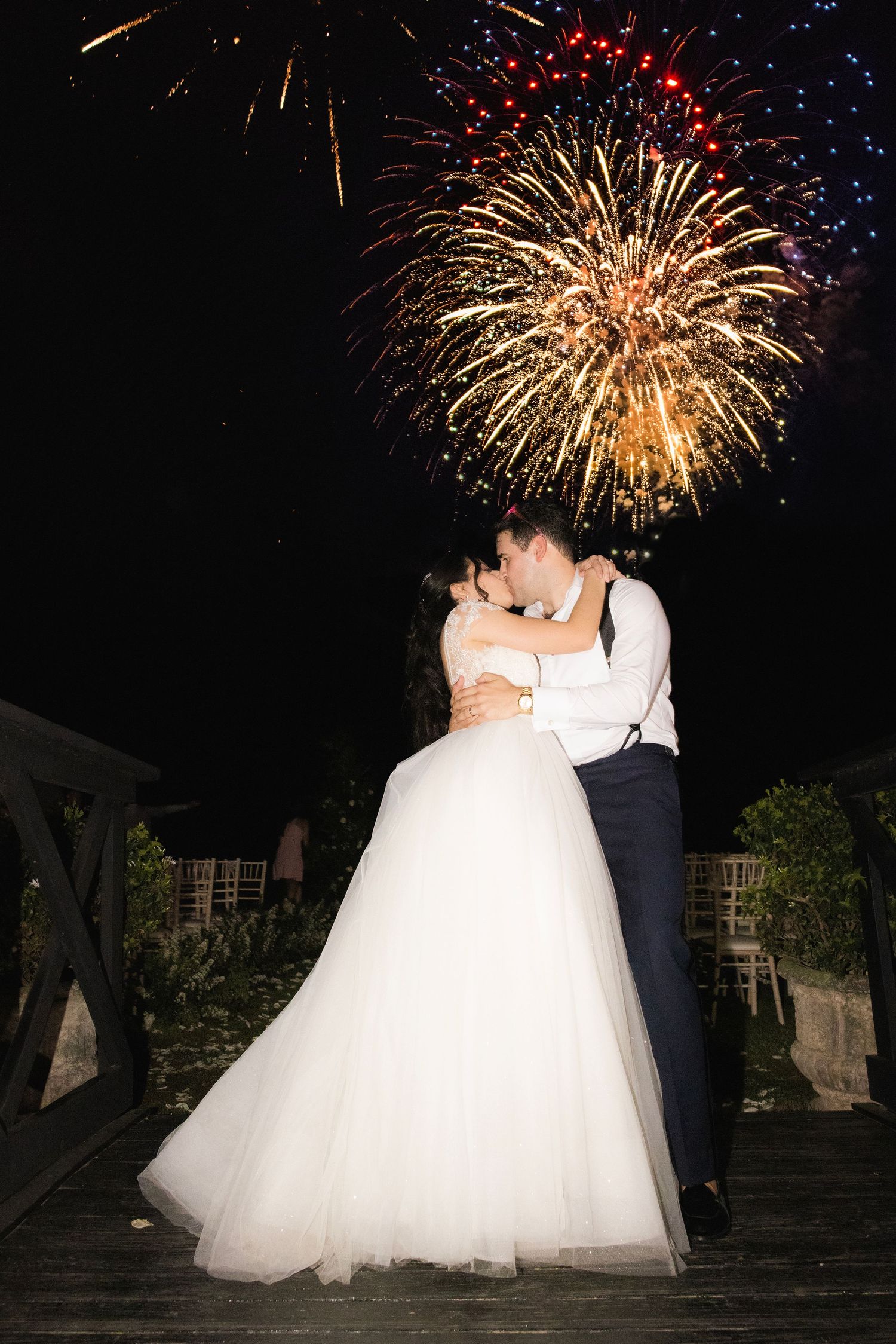 Newlyweds share a romantic moment as colorful fireworks illuminate the night sky during their celebration.