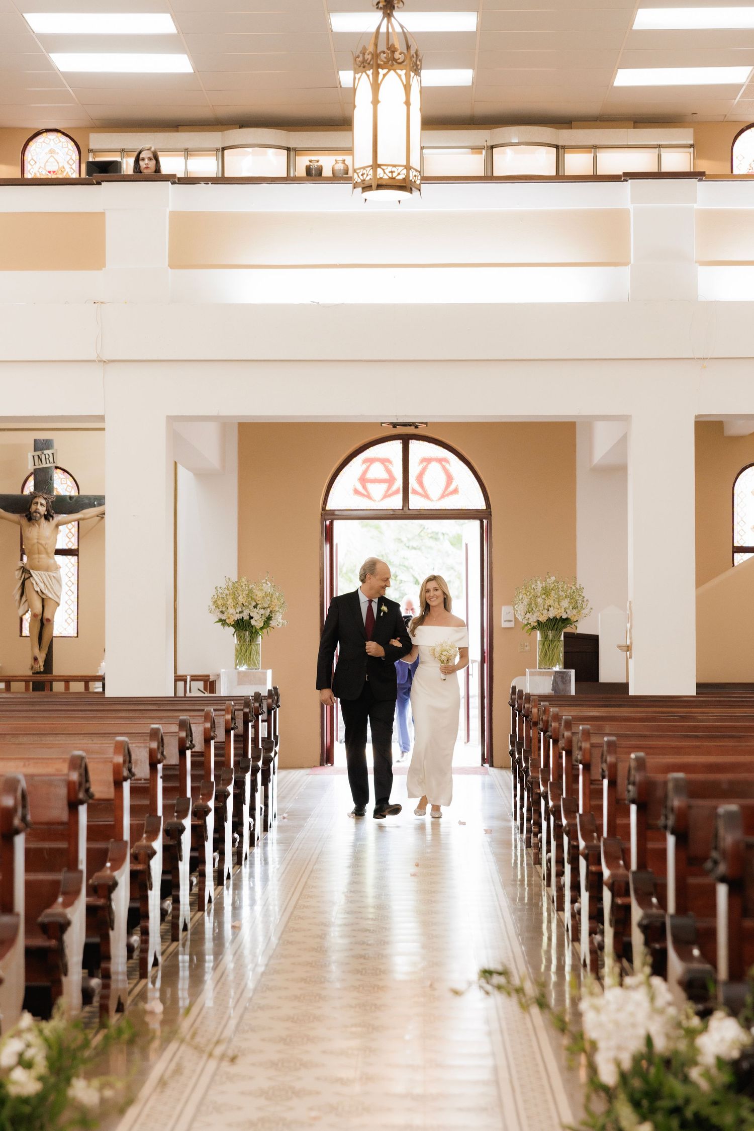 A panoramic sequence showing two figures walking down the aisle of an elegant light-filled church with white floral arrangements.