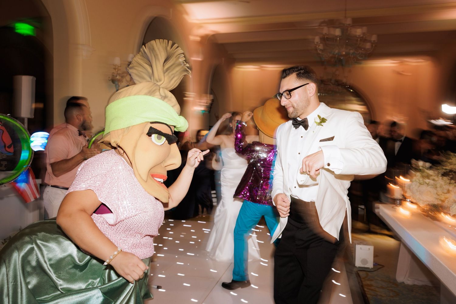 Wide angle view of wedding guests dancing and celebrating in a warmly lit ballroom.