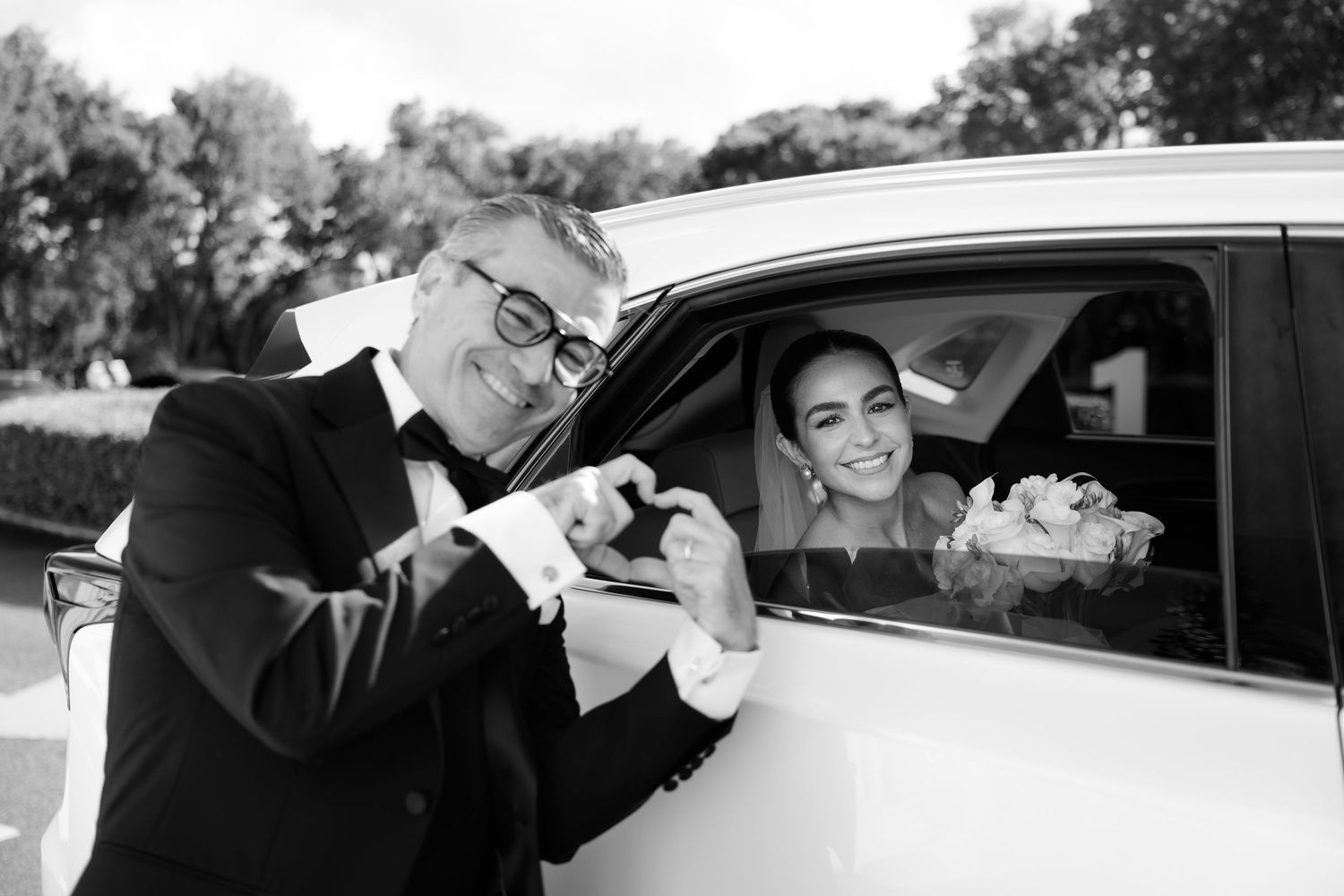 Black and white photo of joyful moments shared between wedding attendees near a car.