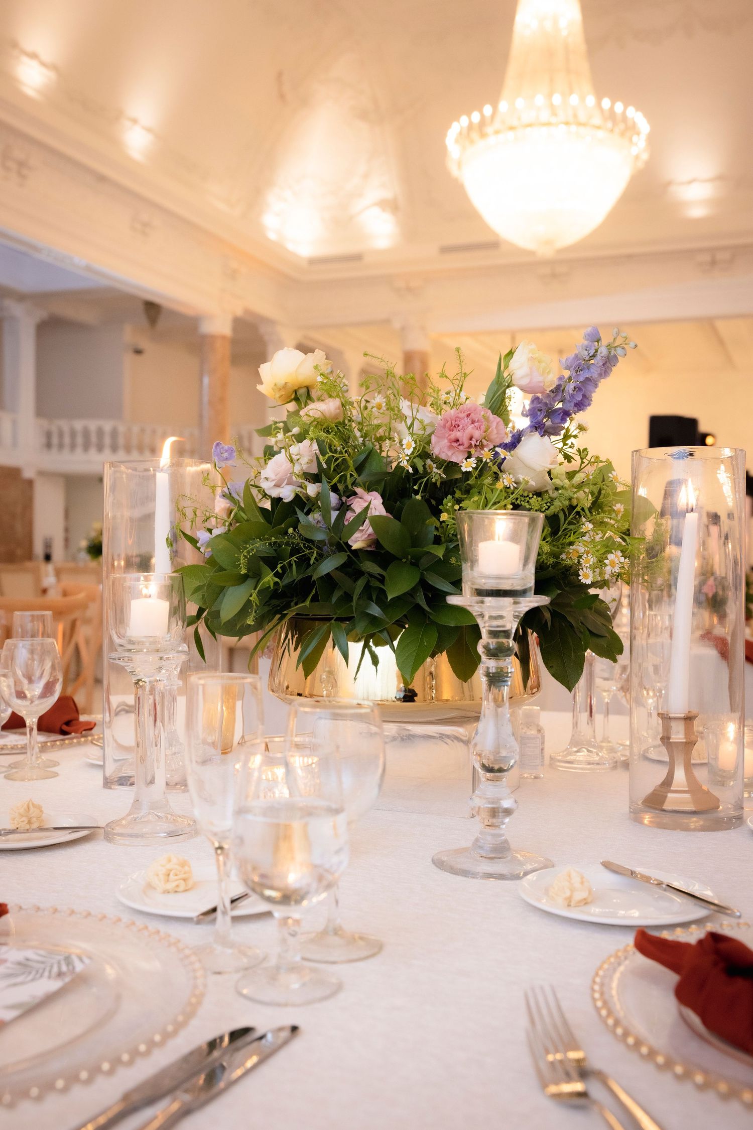 Luxurious wedding reception table setting with floral centerpiece and crystal candle holders under a grand chandelier.