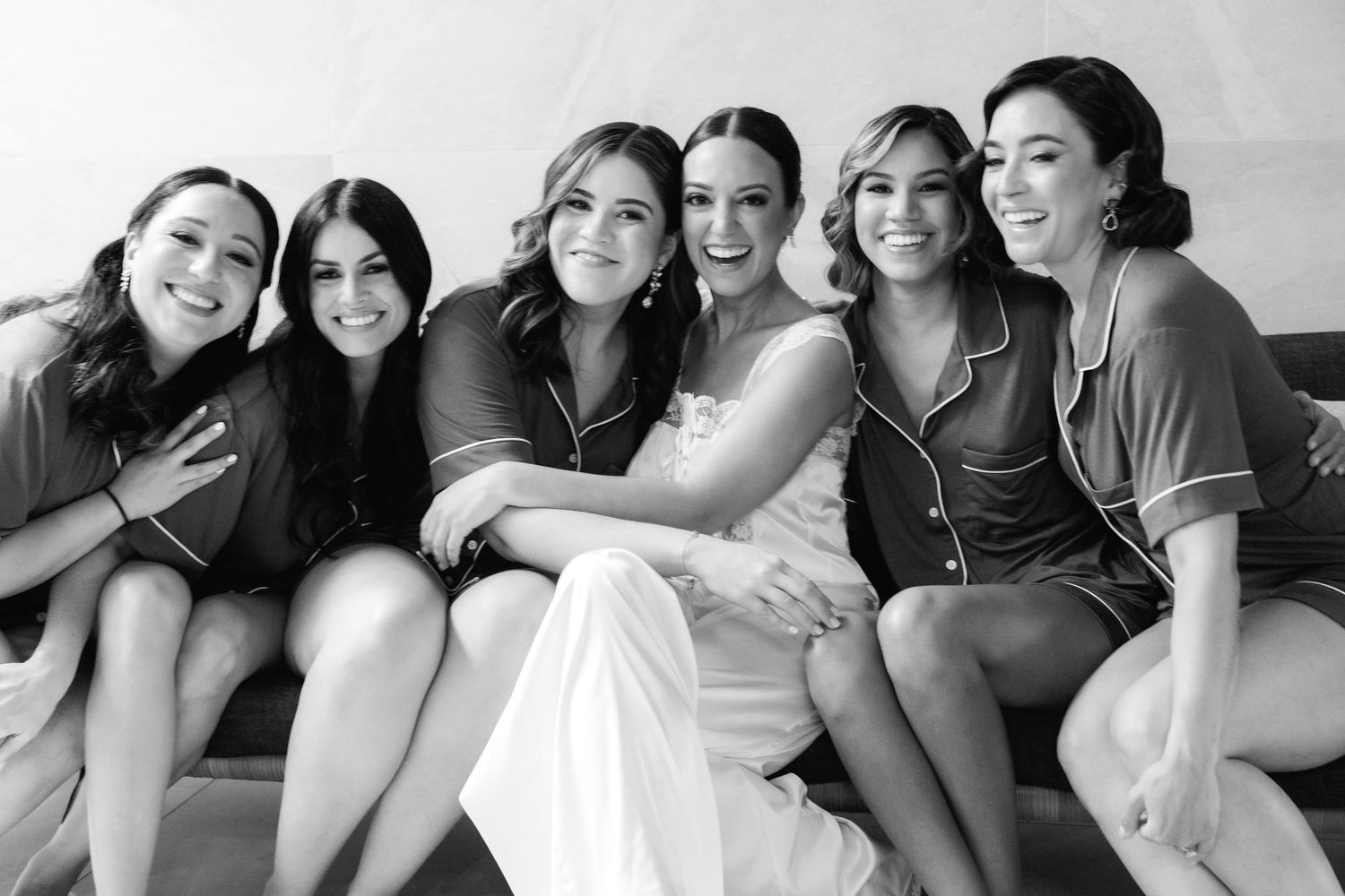Black and white photograph showing a group of six friends smiling and sitting closely together on a couch.