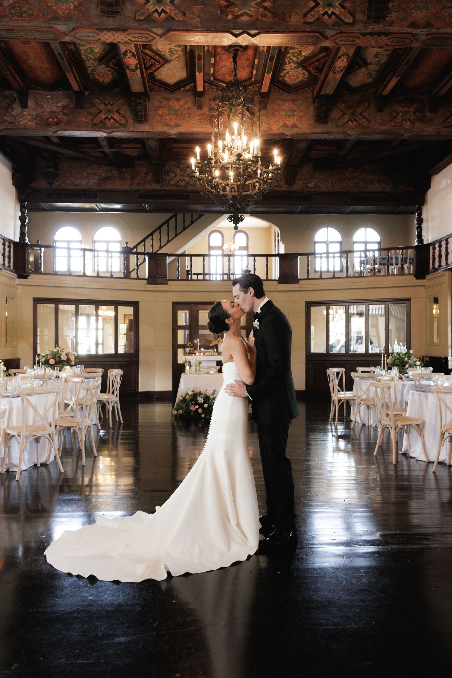 Elegant wedding reception venue with dark wood beams, crystal chandelier and white decor in a grand historic ballroom.
