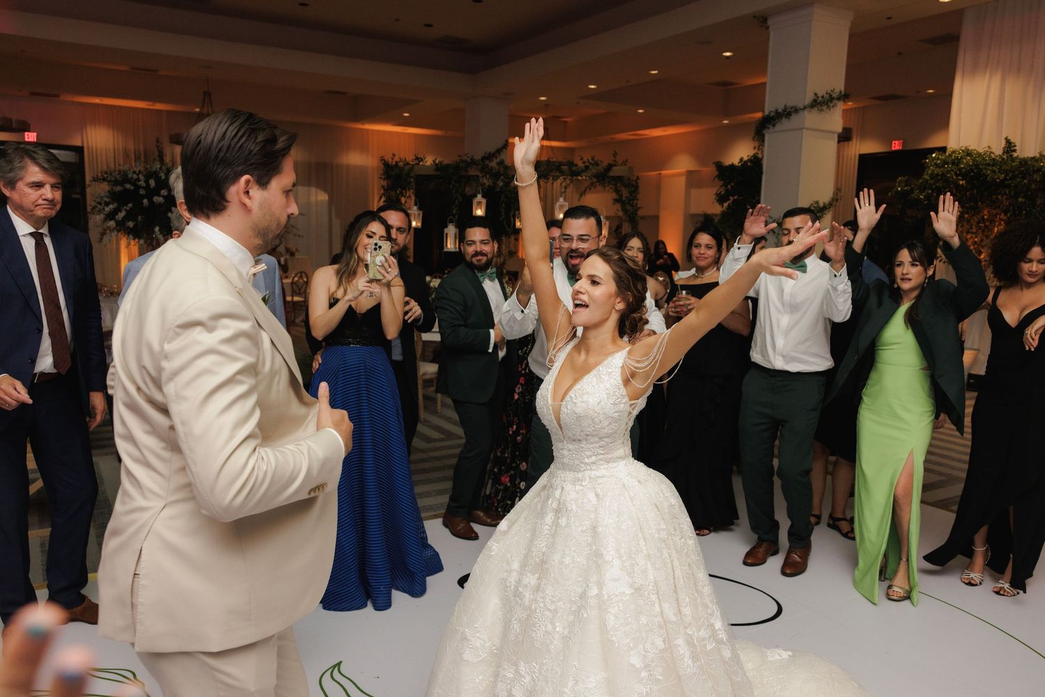 Newlyweds celebrate on dance floor with guests at wedding reception in grand ballroom.