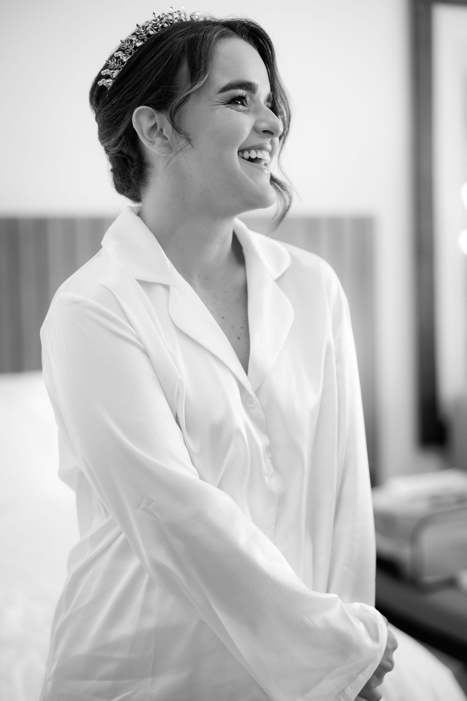 Black and white portrait of someone wearing a white shirt and tiara while smiling warmly to the side.