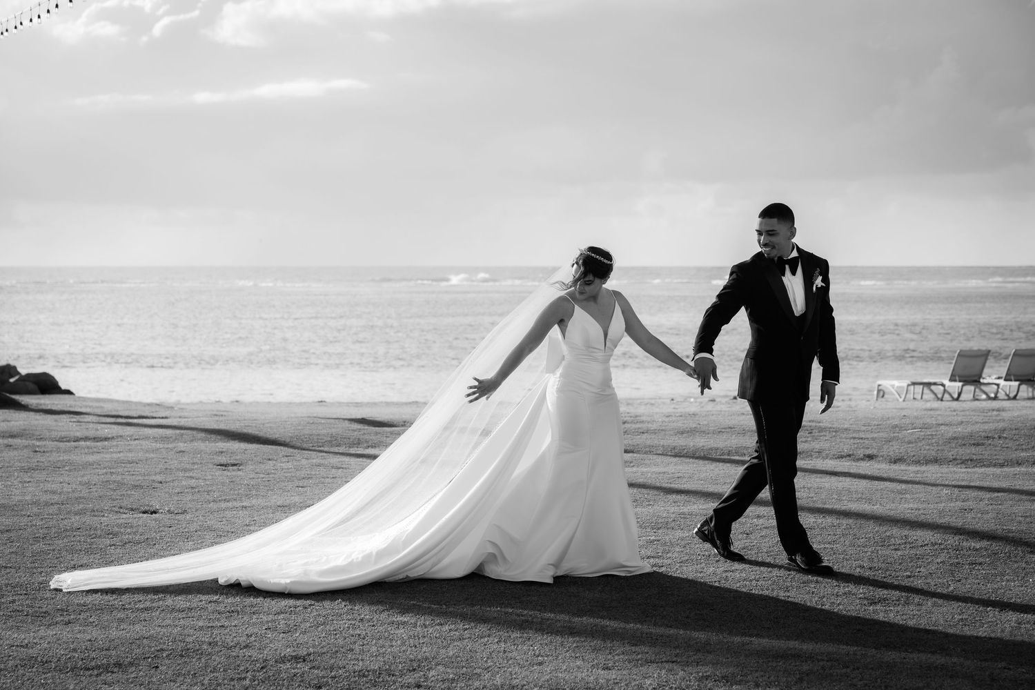 A couple walks along a misty beach with flowing white fabric creating a dramatic silhouette against the ocean background.