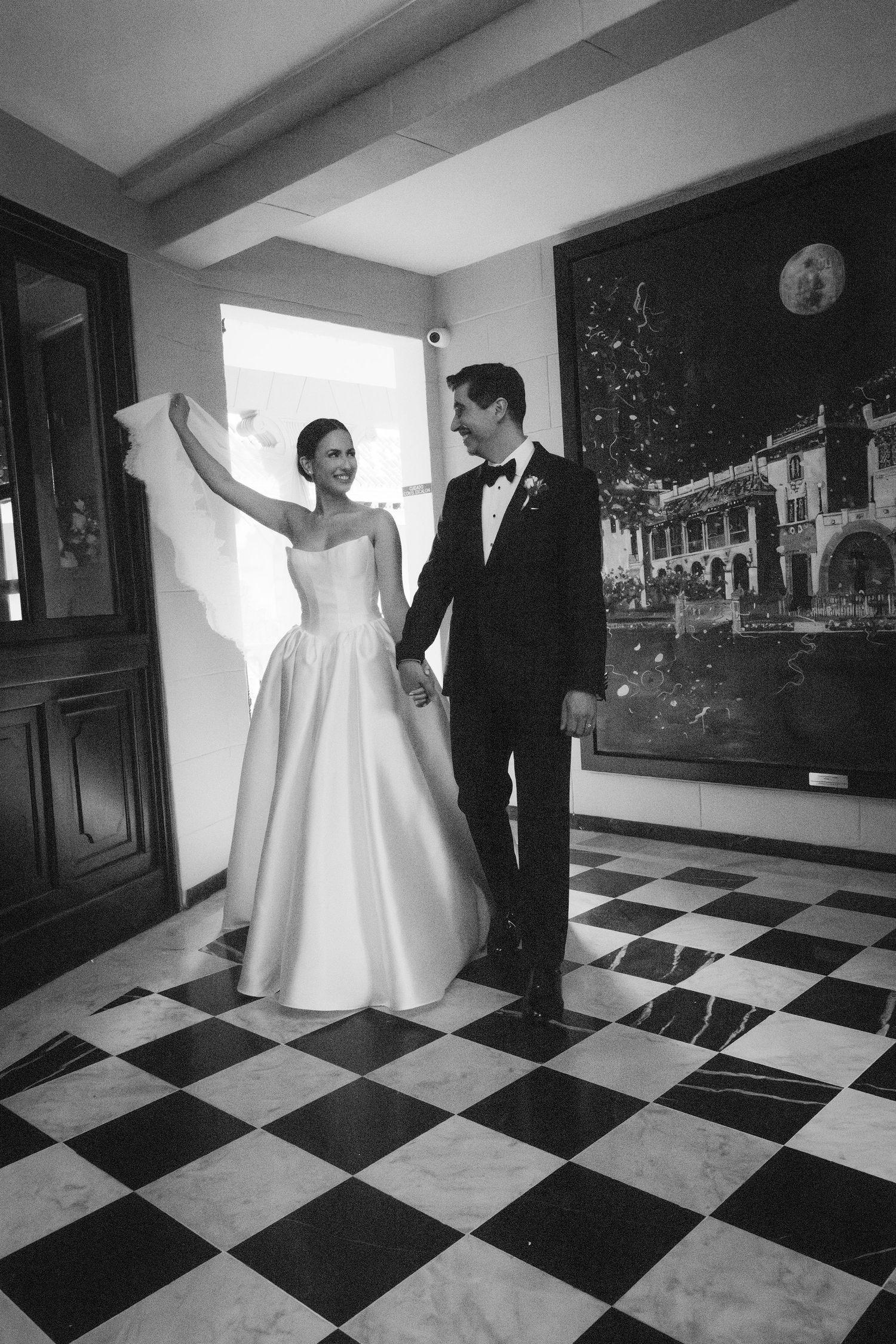 A couple dances on a striking black and white checkered floor in an elegant indoor setting.