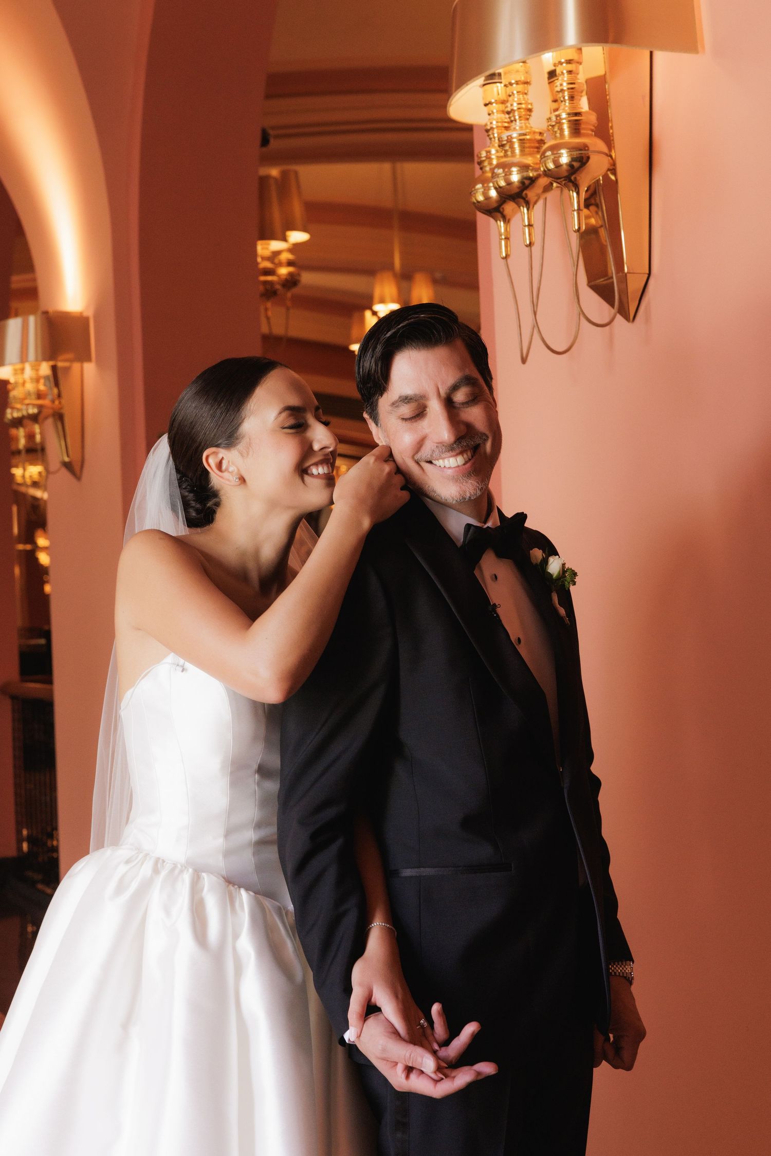 A joyful wedding moment captured in warm lighting with a bride in white dress and groom in black tuxedo.