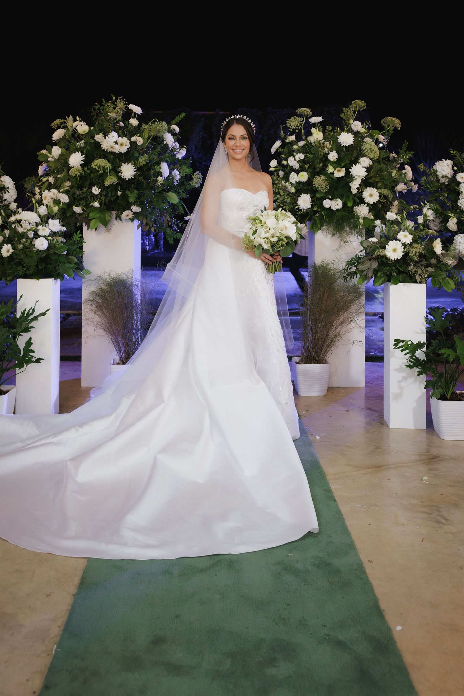 A stunning white wedding gown with a flowing train and veil is displayed among elegant floral arrangements.