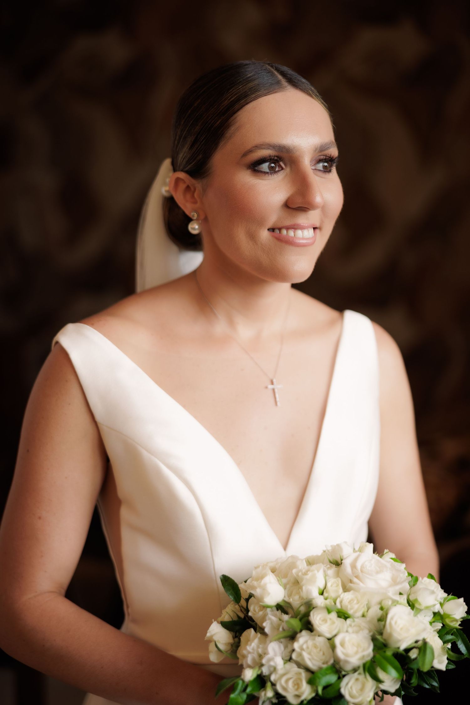 Classic white bridal bouquet with roses and greenery against dark background.