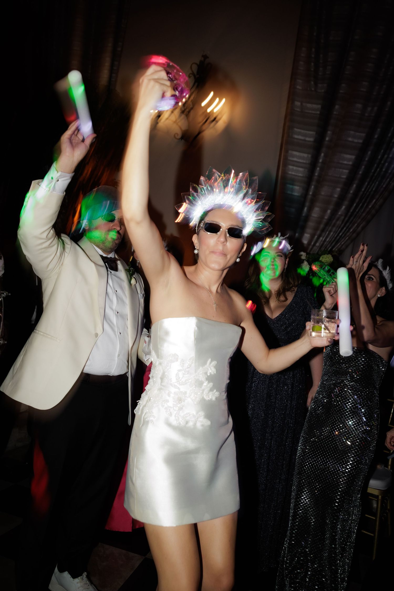 People dancing and partying in a dark nightclub setting with colorful lights and white outfits.