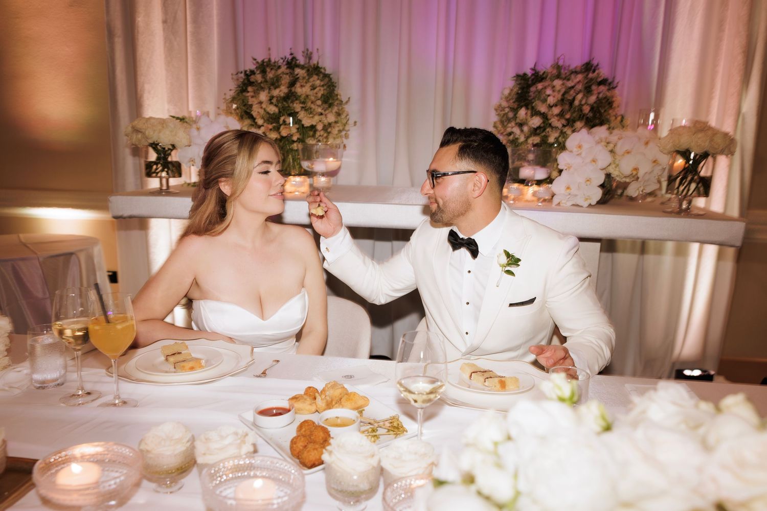 Wedding reception dining tables decorated with floral centerpieces and white linens in an elegant ballroom setting.