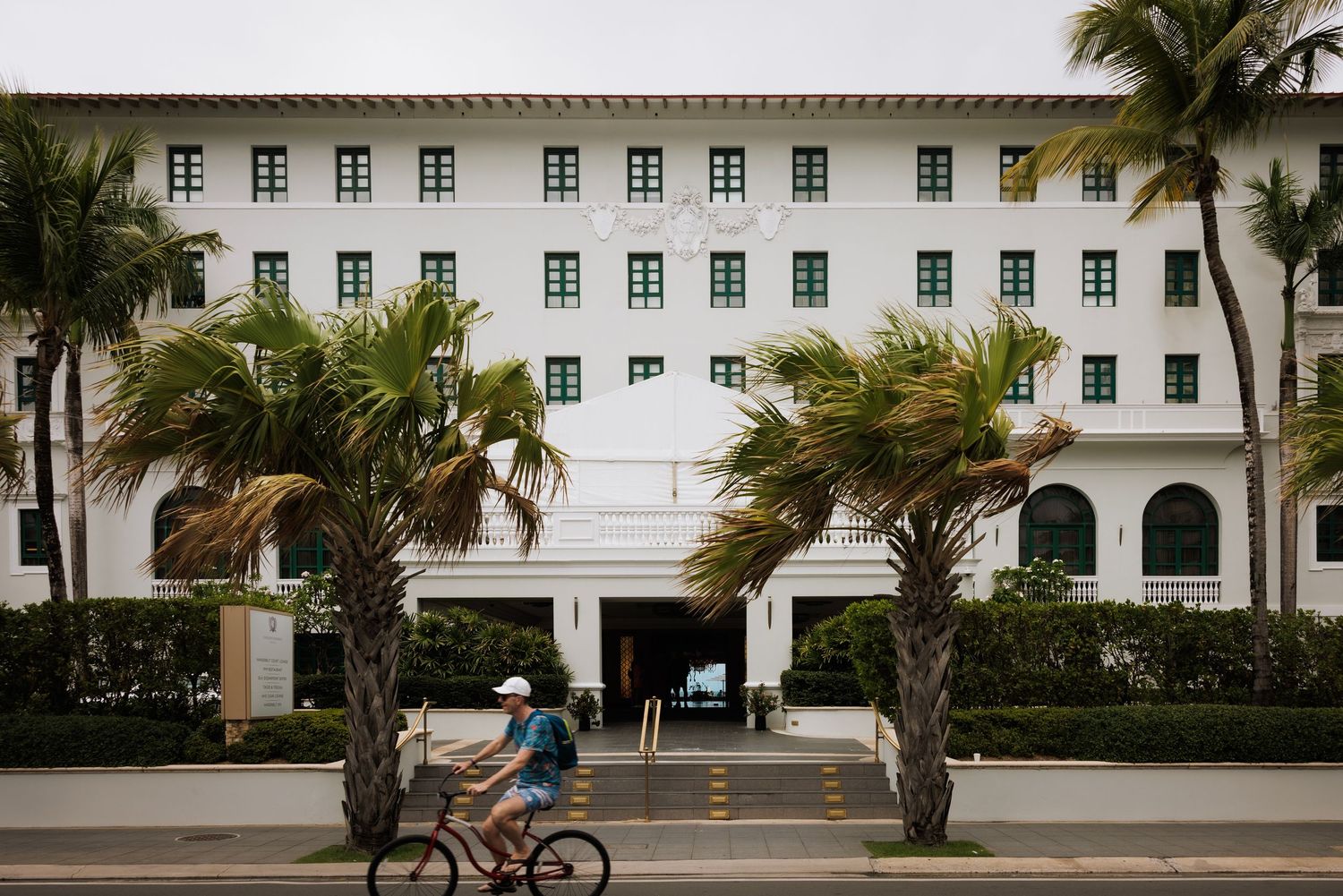 White colonial style building with palm trees and walkways on a university or resort campus in tropical setting.