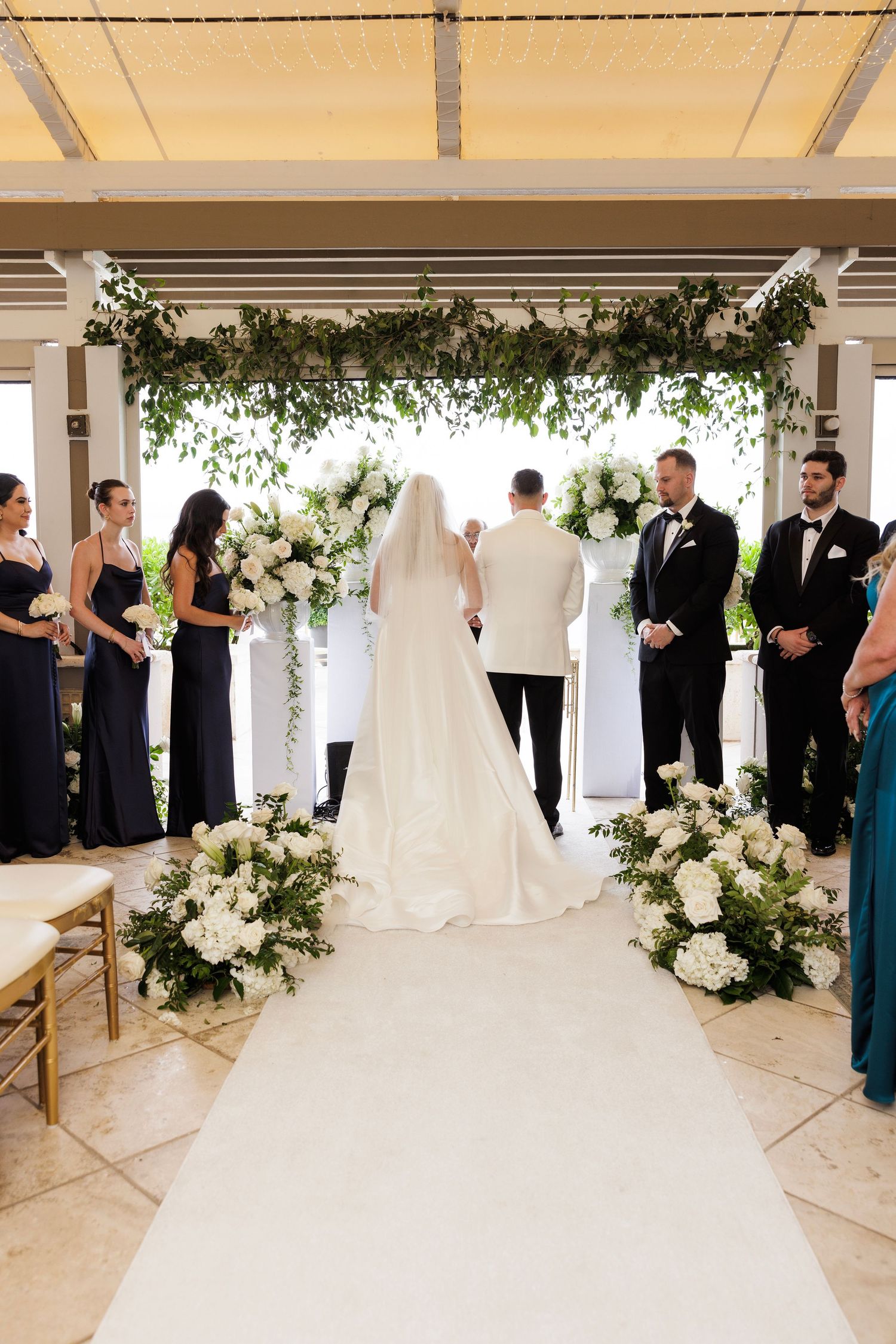 Elegant outdoor wedding ceremony setup with white floral arrangements and covered pavilion.