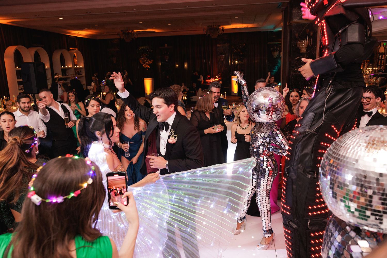 Wedding reception guests dance and celebrate in a dimly lit ballroom with a disco ball overhead.