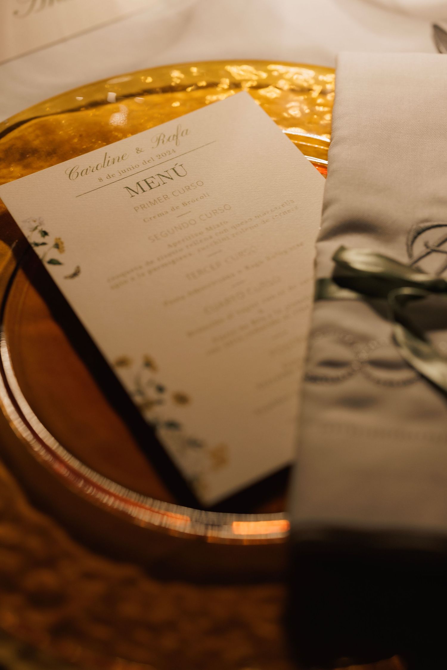 Close-up view of elegant wedding menu cards with decorative calligraphy displayed on a reflective copper surface.