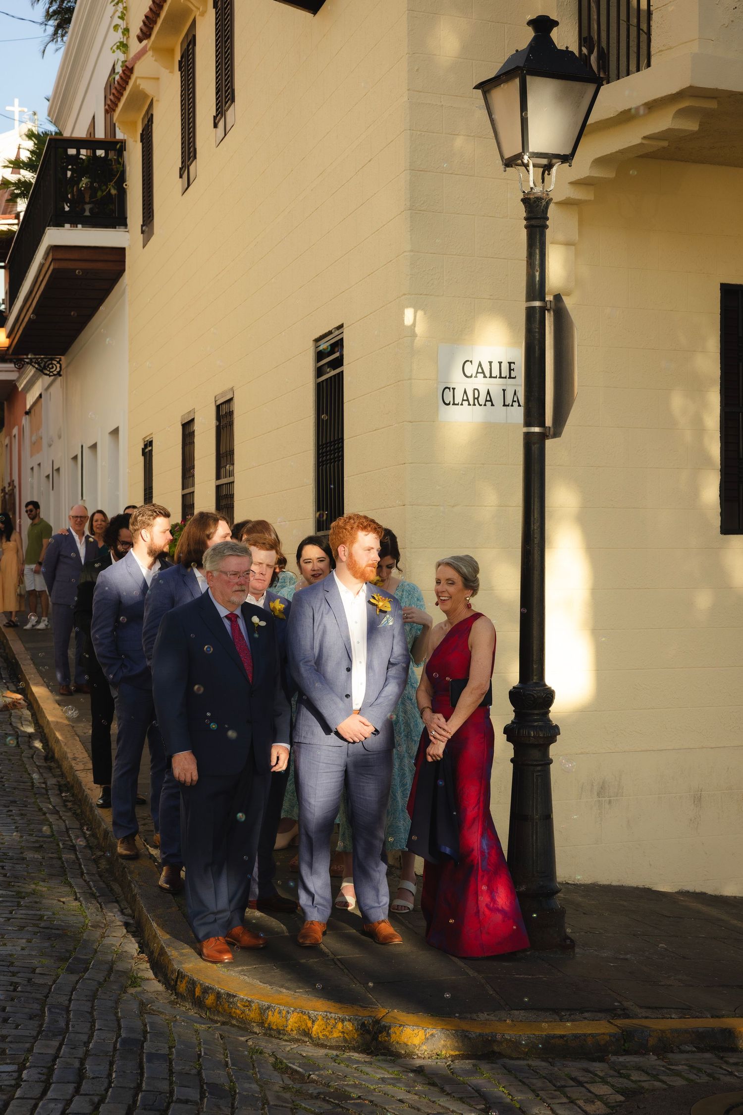 Wedding party gathers along a charming colonial street with yellow walls and cobblestones.
