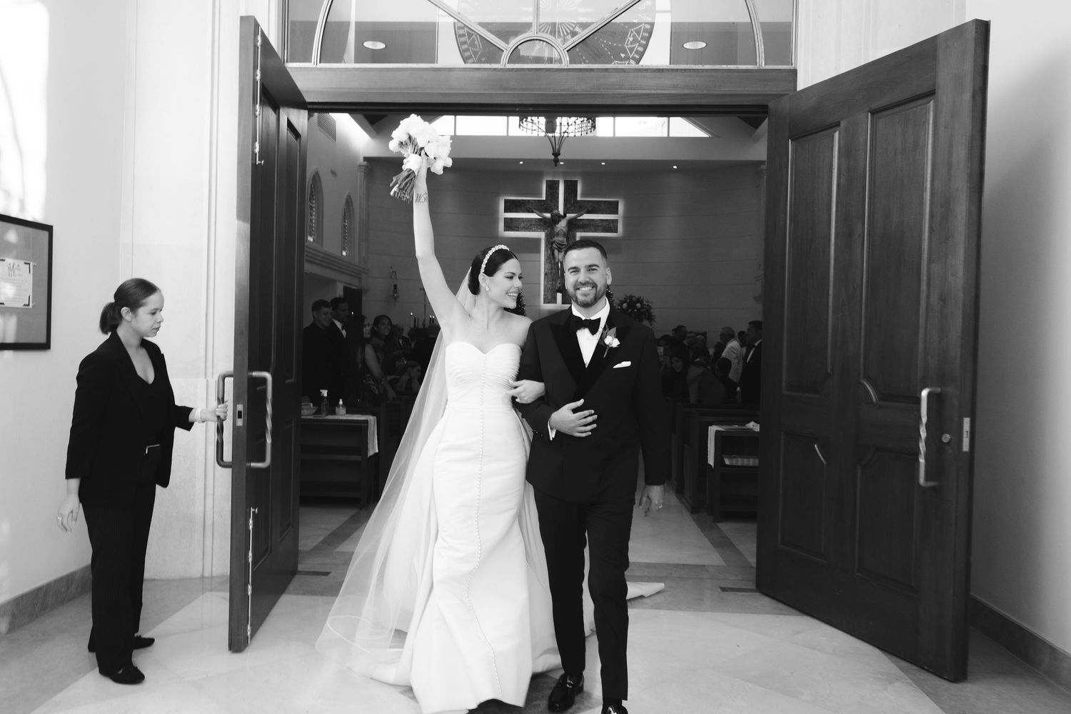 A joyful couple celebrates while walking through large double doors after their wedding ceremony.