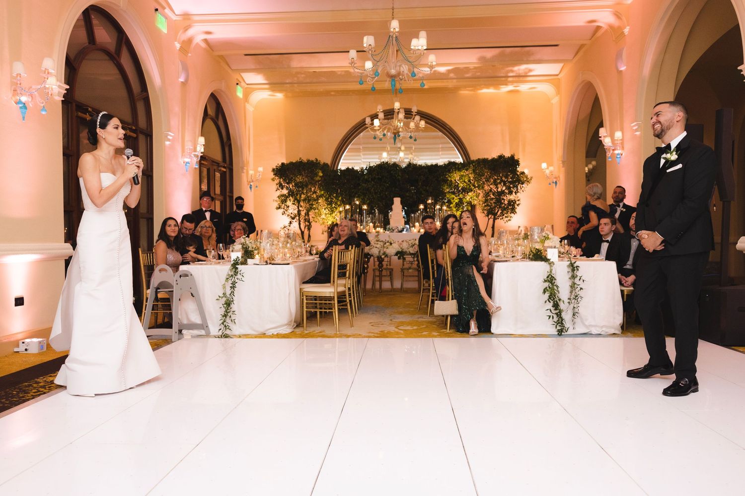 An elegant wedding ceremony setup in a grand ballroom with white decor, arched doorways and a crystal chandelier.