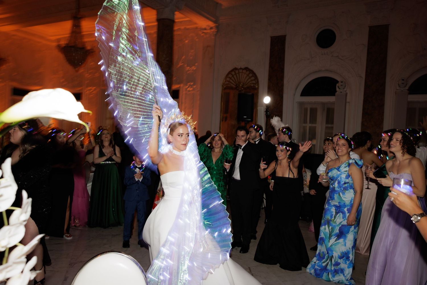 Wedding guests celebrate on the dance floor at an evening reception as glowing lights illuminate the venue.