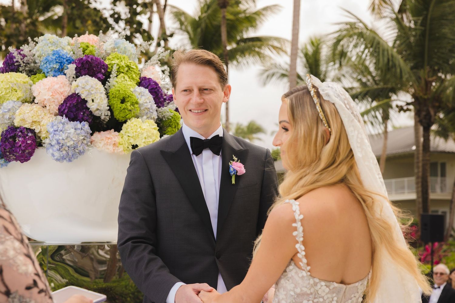 A seaside wedding reception features colorful floral arrangements and tropical palm trees in the background.