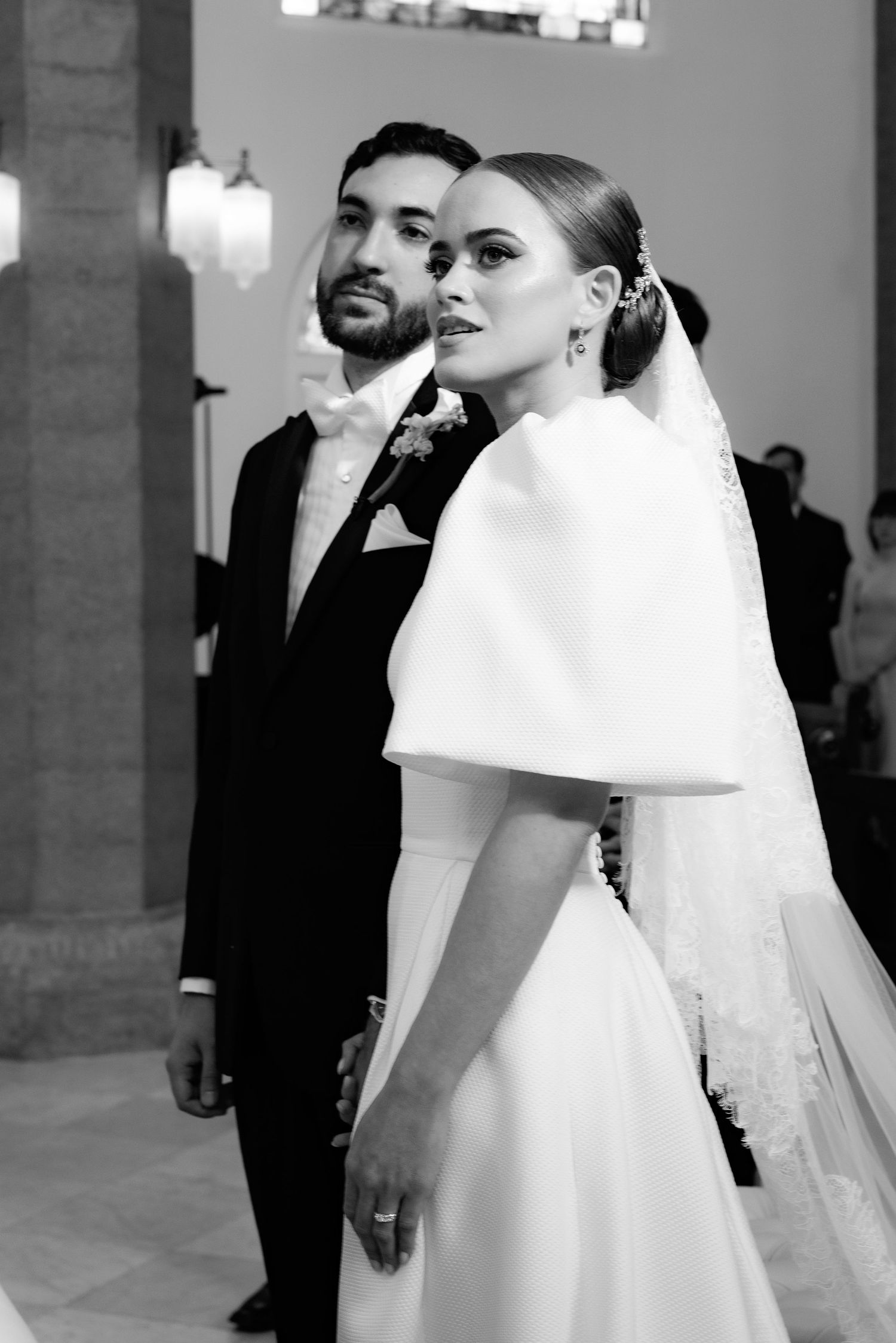 Classic black and white wedding portrait with bride in white dress with cape detail and veil beside groom in tuxedo.