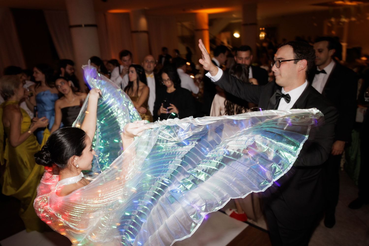 A colorful LED light display at an event creates a dynamic wave pattern in a dark room with attendees watching.