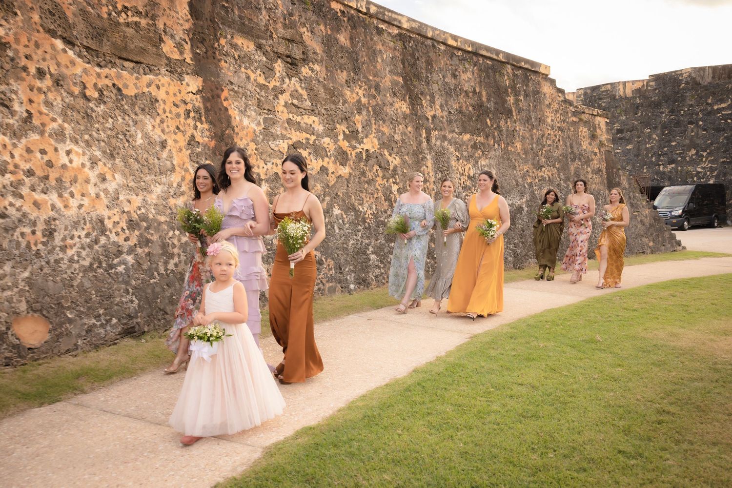 Wedding party walking along historic stone fortress walls during sunset.