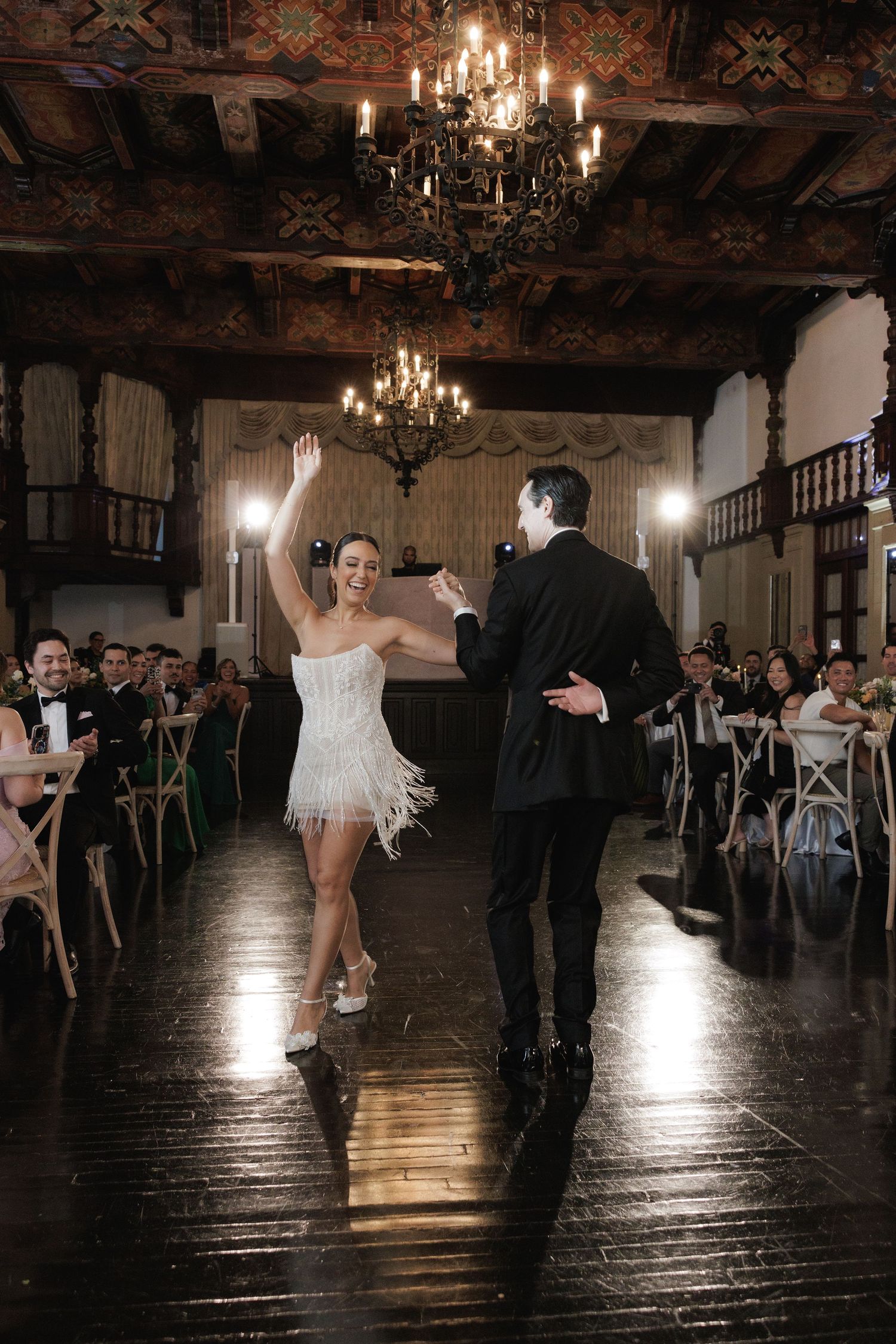 A dramatic dance performance unfolds on a polished ballroom floor beneath ornate chandeliers.