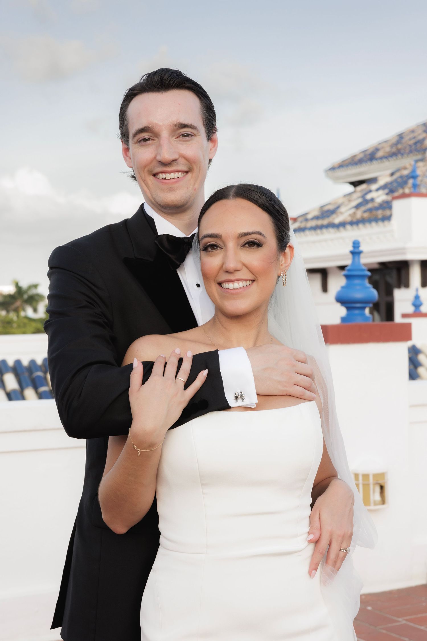 A newlywed couple embraces on a white rooftop with decorative blue details and architecture in the background.