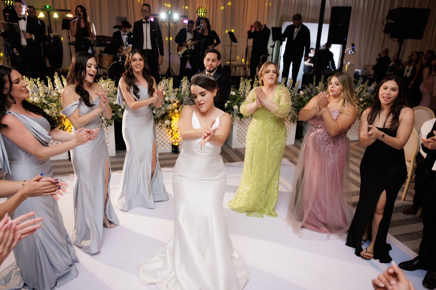 Celebration on a white dance floor at an elegant wedding reception with guests in formal attire dancing and mingling.
