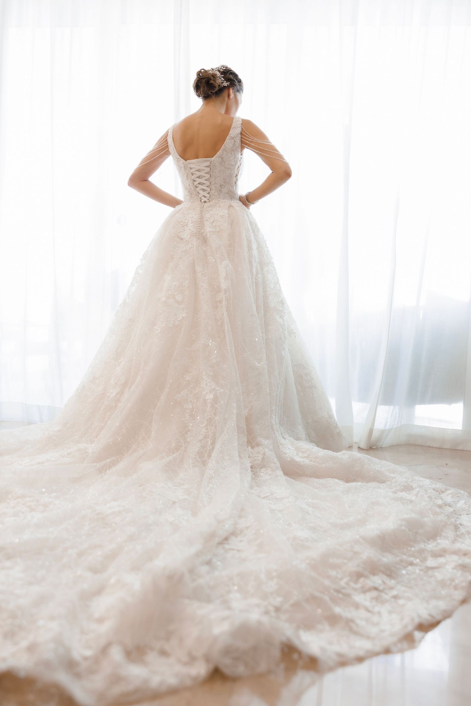 Elegant white wedding gown with lace corset back and dramatic cathedral train shown from behind in natural light.