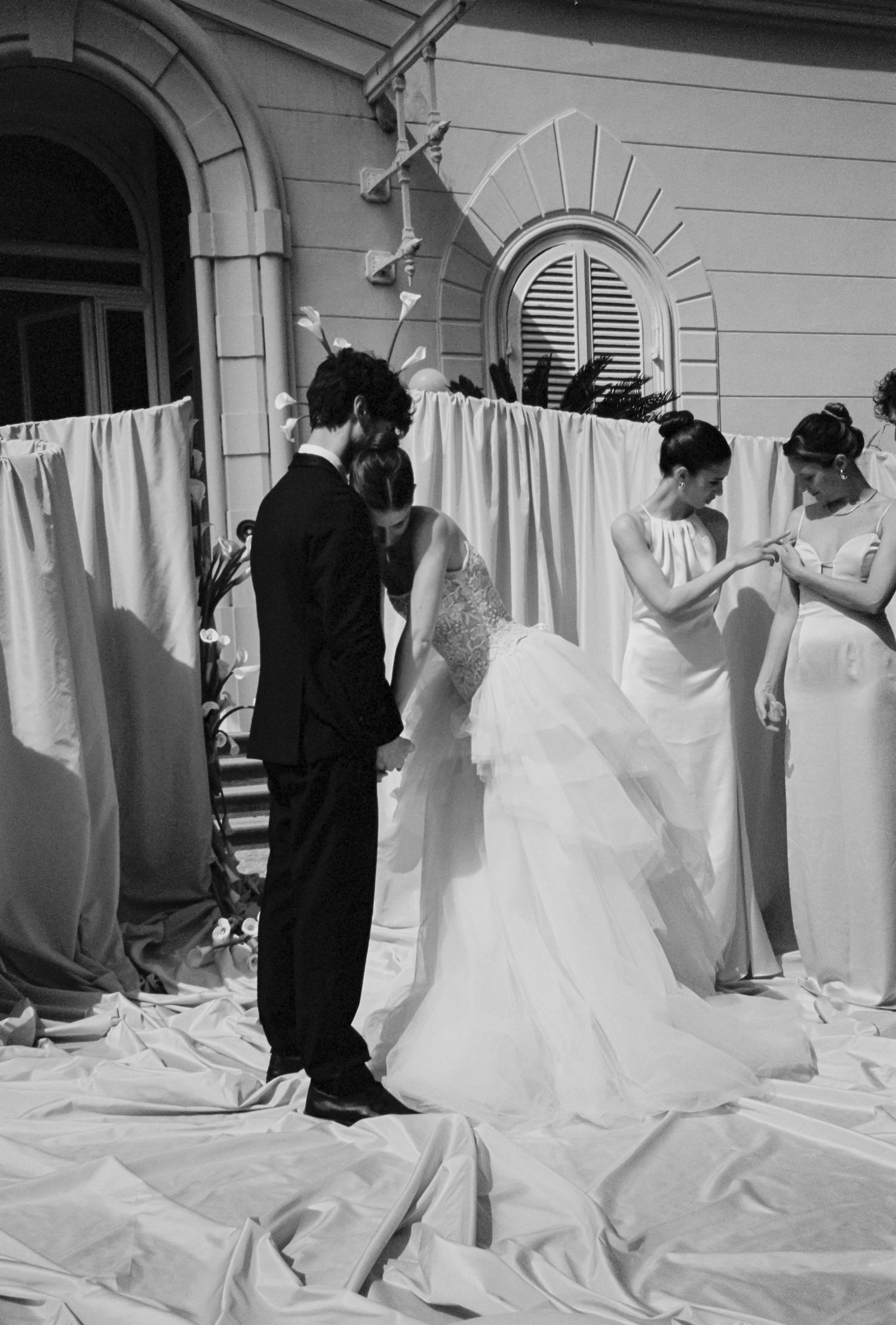 Black and white photo of a bride and groom exchanging vows outdoors, attended by bridesmaids in elegant gowns.