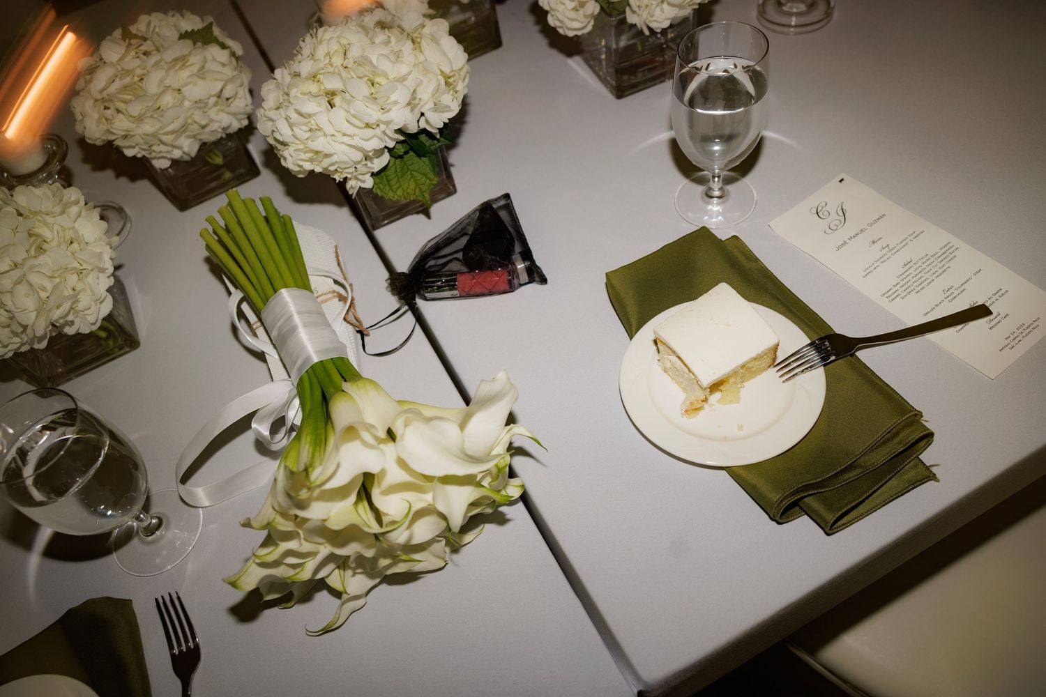 Elegant table setting with white hydrangeas, wine glasses, and menu cards on olive green napkins.