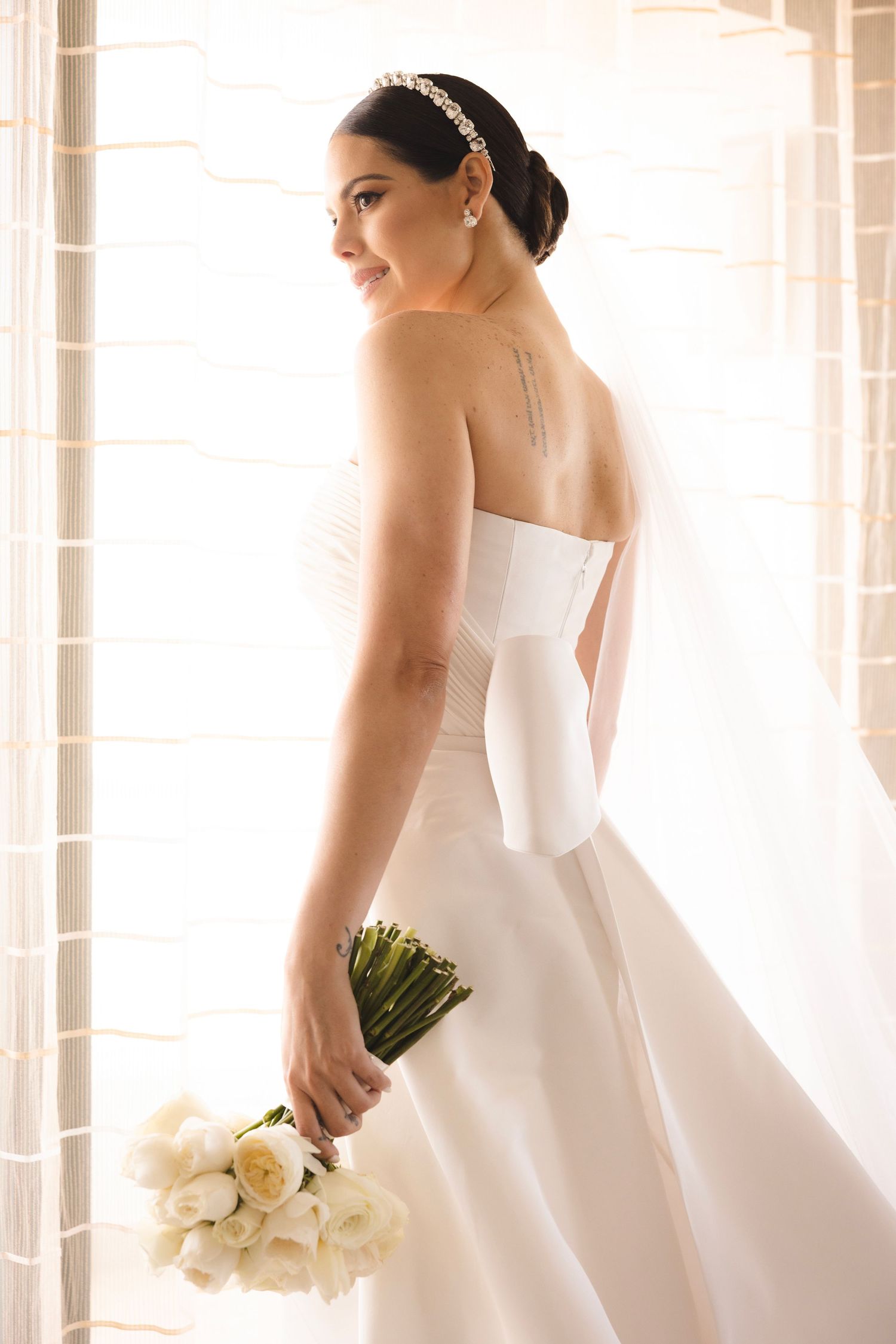 Elegant bridal portrait showcasing white wedding dress details and delicate bouquet near sunlit window.
