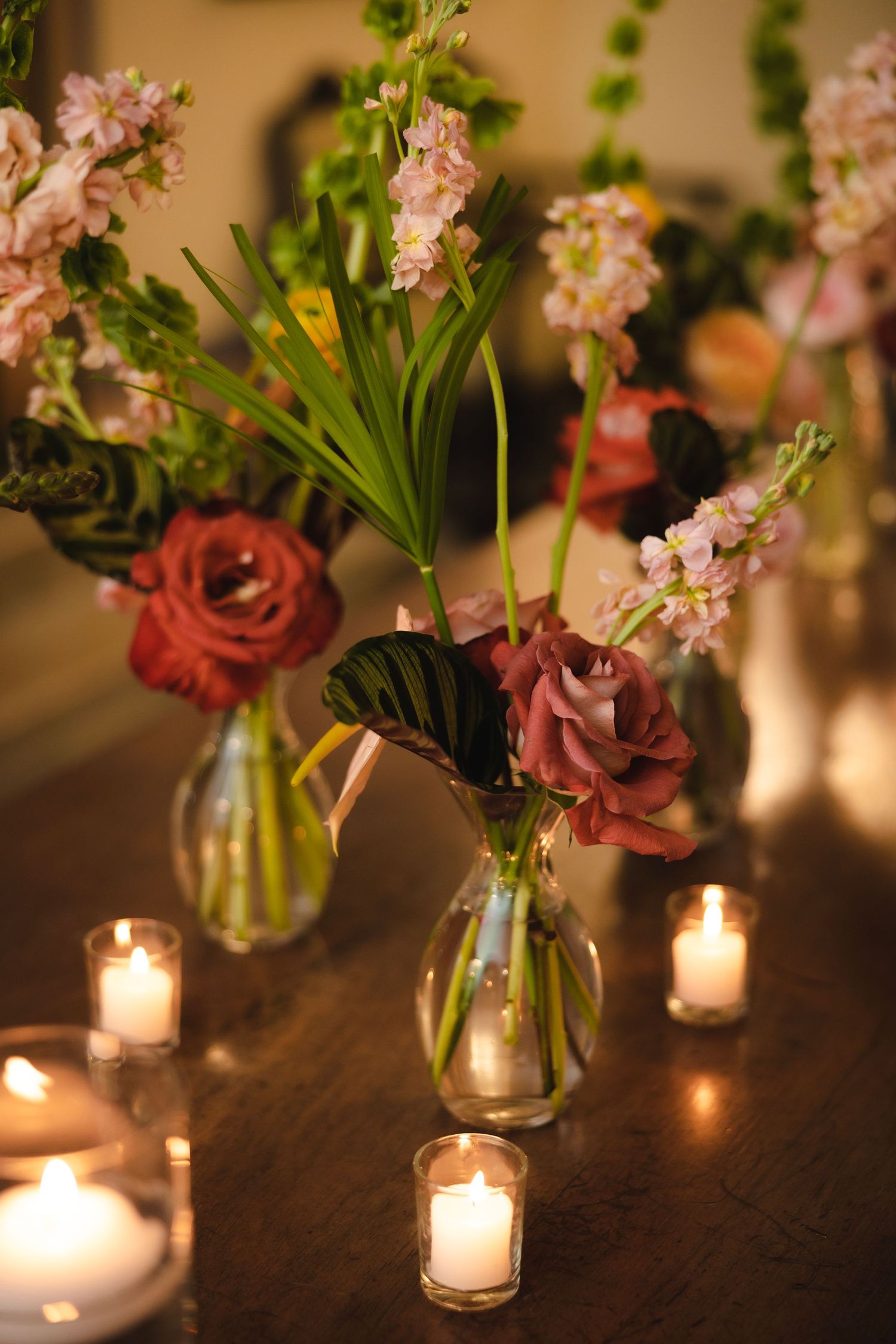 Pink and coral roses arranged in glass vases with glowing candles create an intimate romantic table setting.