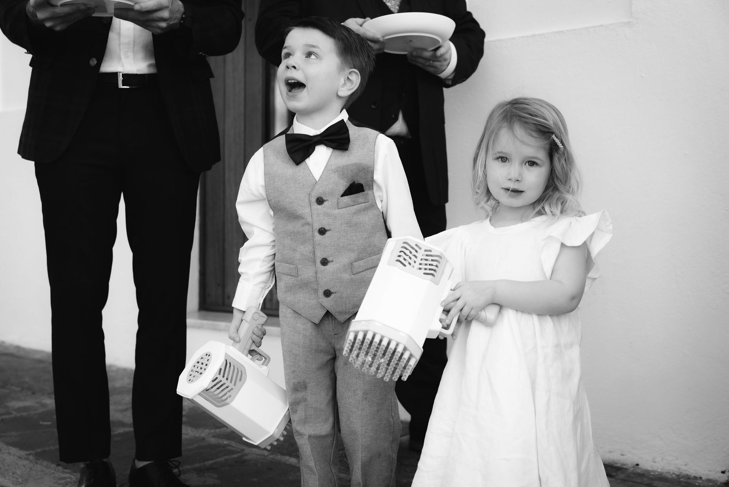 Young wedding attendants in formal attire holding ceremony programs in a black and white photograph.