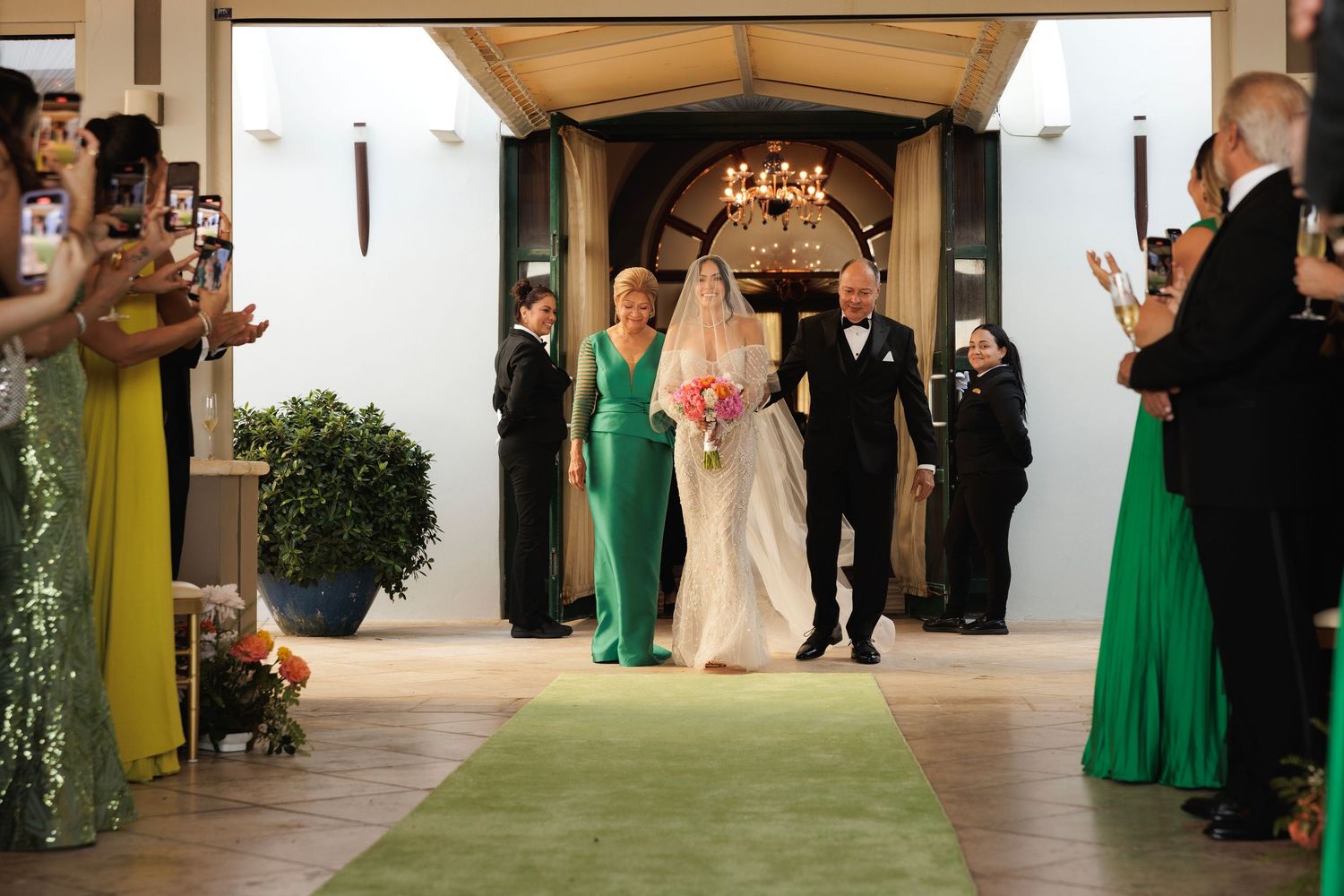 Wedding party members in emerald green dresses and black suits line up in an elegant hallway during reception.
