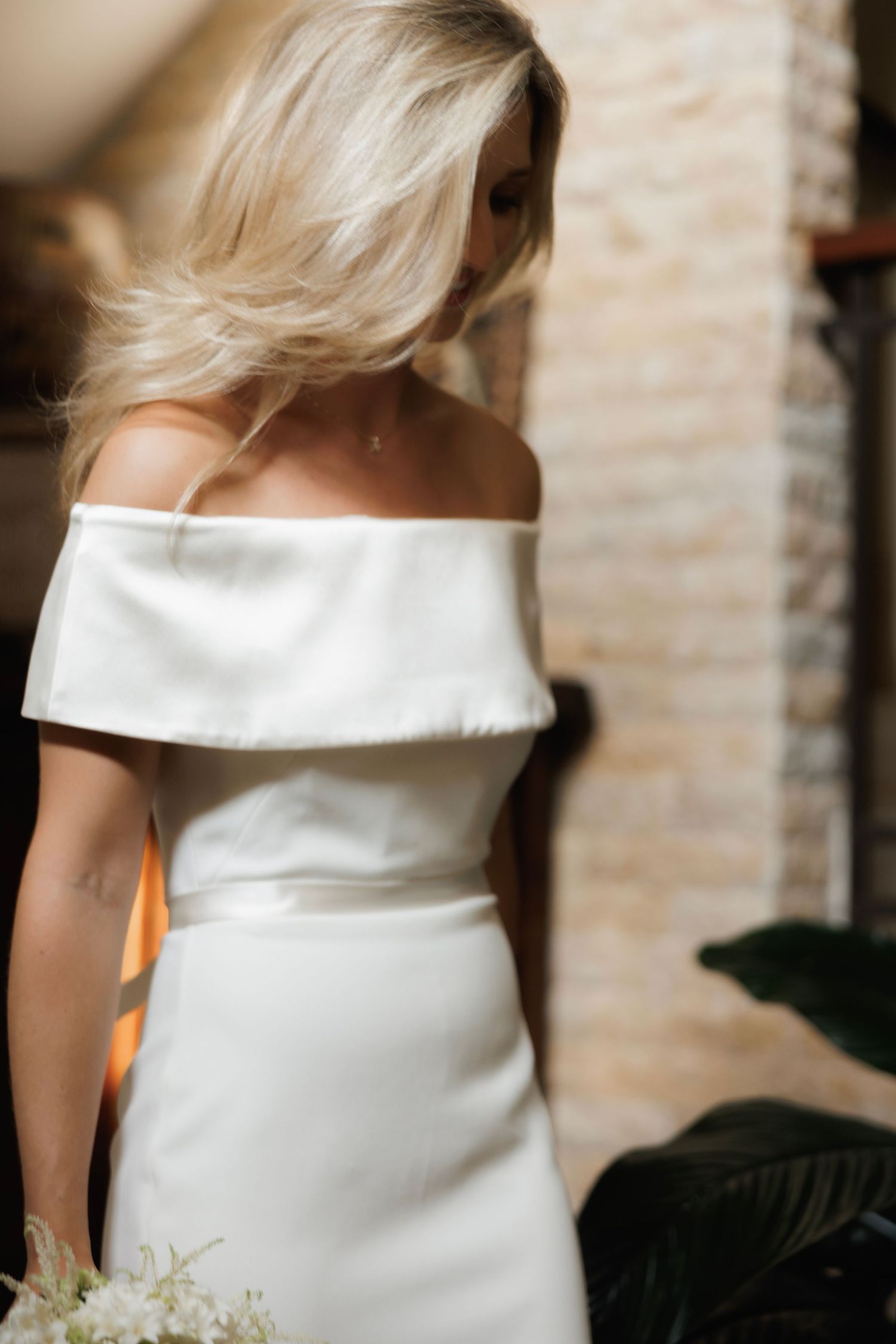 A close-up sequence showing details of an elegant off-shoulder white wedding dress against a stone wall background.