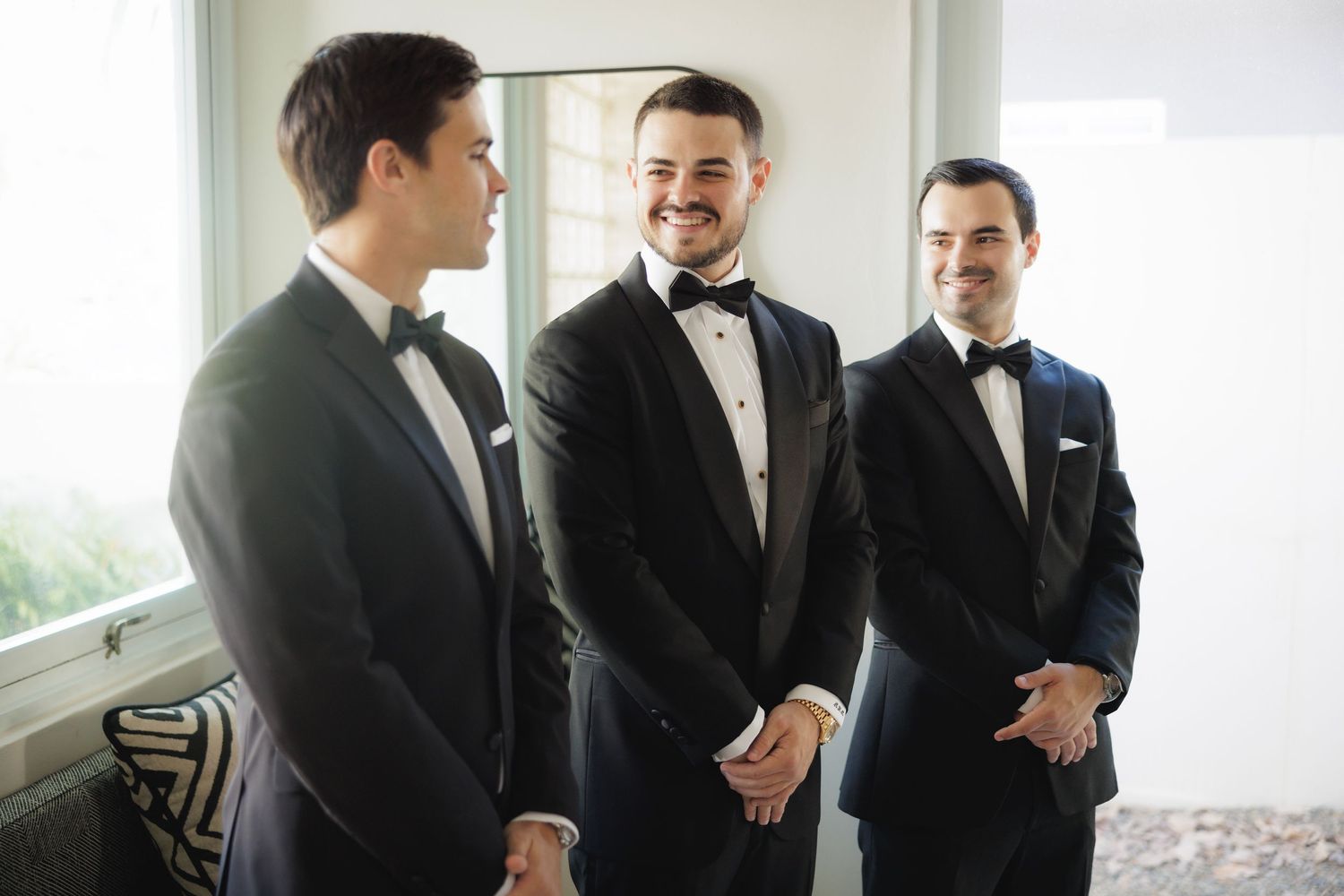 Groomsmen in black tuxedos share candid moments and laughs before the wedding ceremony.