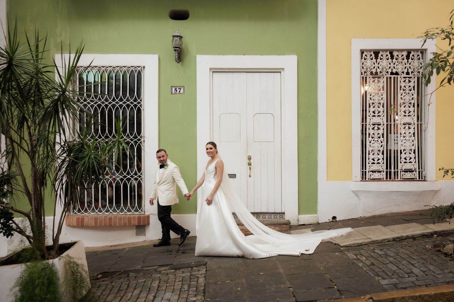 A wedding couple walks down a colorful street with ornate iron window bars and a palm plant in Old San Juan.