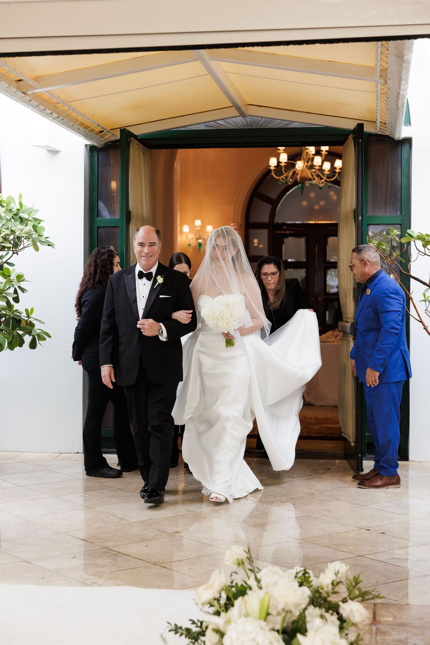 Wedding party entering through an arched doorway with white floral arrangements.